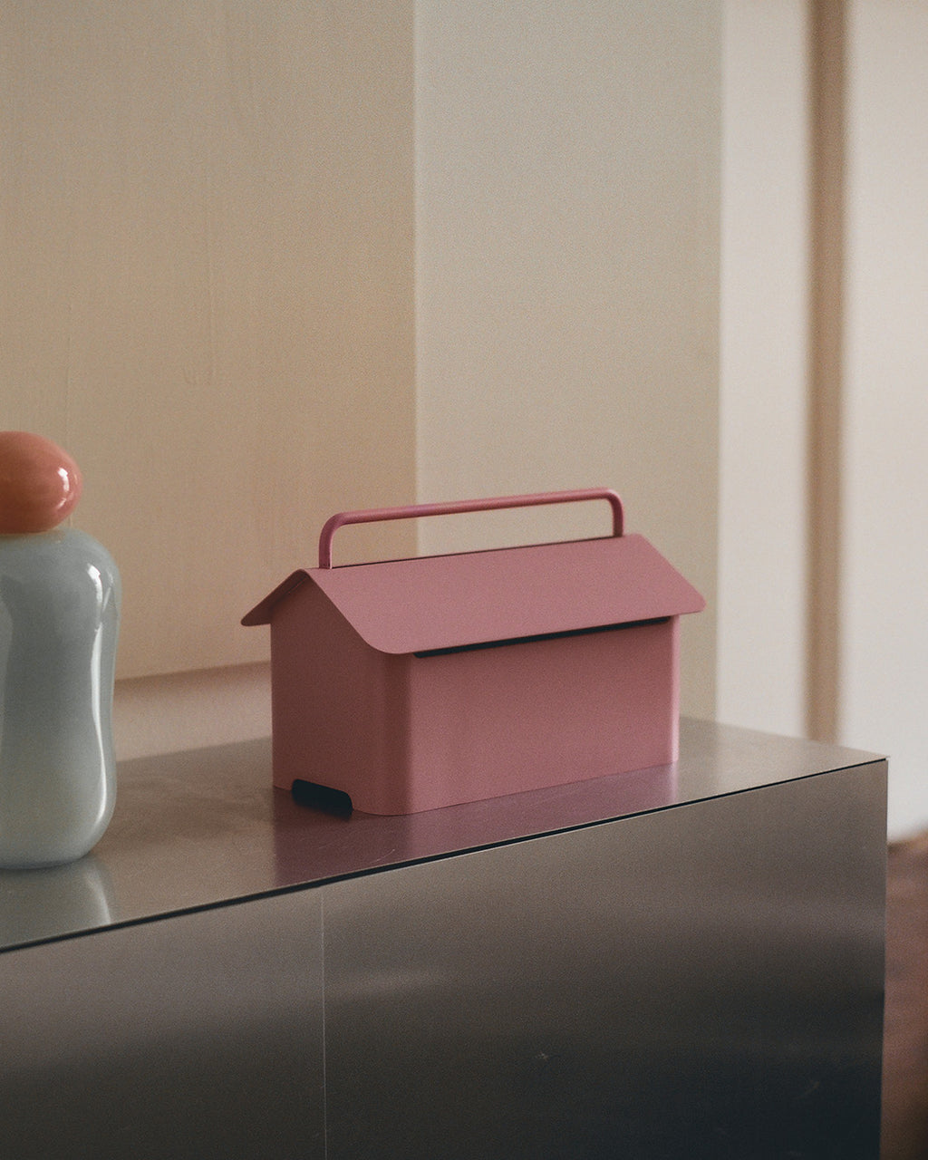 Cable Villa in Bubble Gum posé sur un meuble en inox, scène lifestyle avec vase clair et mur beige en arrière-plan