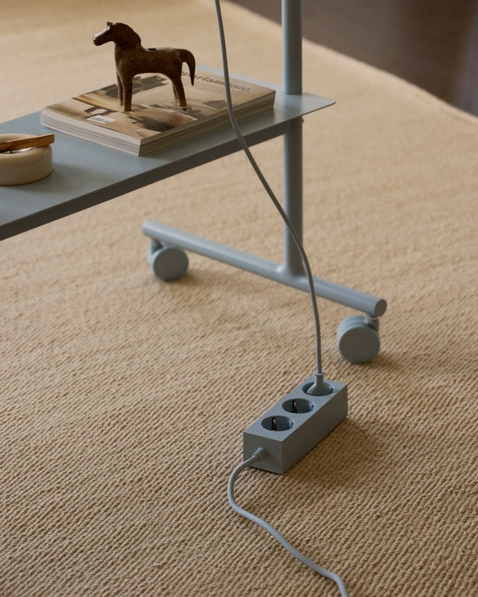 Rover in Powder Blue en scène sur un tapis beige, roulettes visibles, multiprise et câbles au sol
